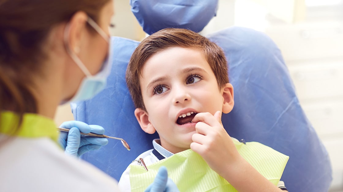 child in dental chair pointing to tooth